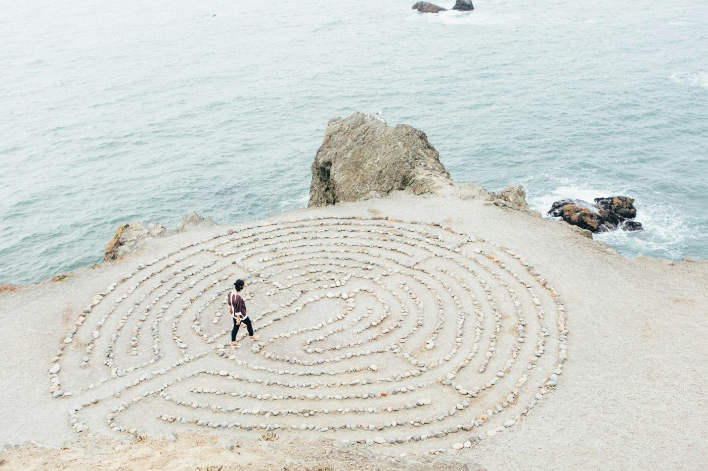 A person walking a stone labyrinth on a coastal cliff